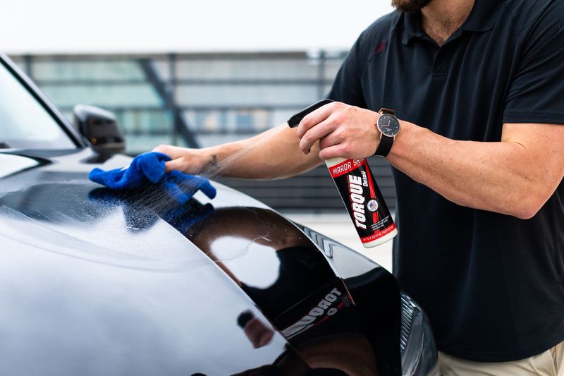 Detailer polishing the red paint of a car with a machine polisher